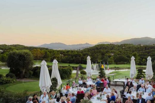 Dîner en plein air, tables rondes, paysage verdoyant et montagnes au coucher du soleil.