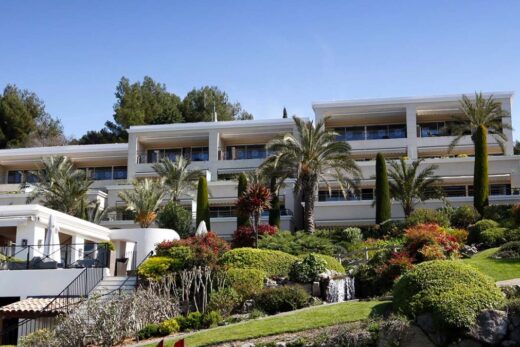Immeuble moderne surplombant jardin entretenu avec palmiers et cascade par jour ensoleillé.