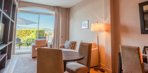 Séjour lumineux, meubles clairs, fenêtre donnant sur patio avec vue sur les montagnes.