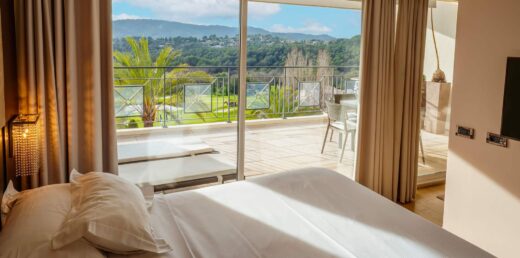 Chambre lumineuse, literie blanche, balcon avec vue pittoresque sur paysage boisé et collines en arrière-plan.