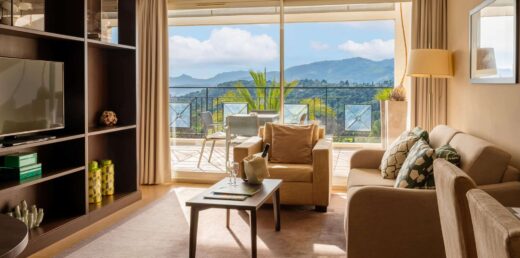 Séjour spacieux avec canapé, fauteuil, table basse. Le balcon avec sièges extérieurs donne sur les montagnes.