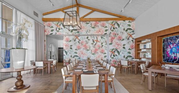 Salle à manger lumineuse, tapisserie florale, tables en bois ordonnées.
