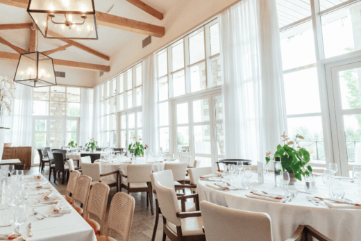 Salle à manger lumineuse avec tables dressées, grandes fenêtres et plantes vertes.