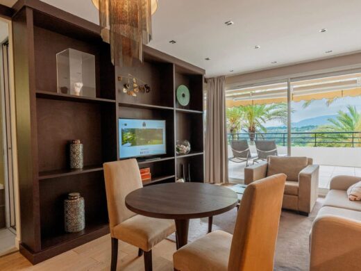 Salon moderne avec table ronde, accès balcon, vue sur mer et palmiers.