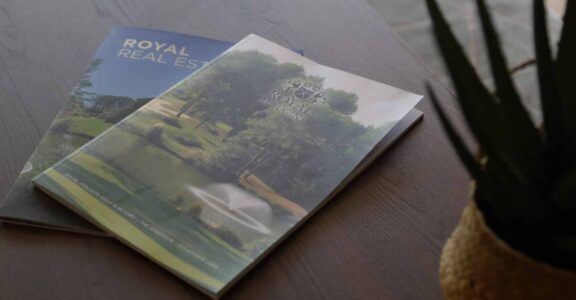 Deux magazines immobiliers sur table près d'une plante.