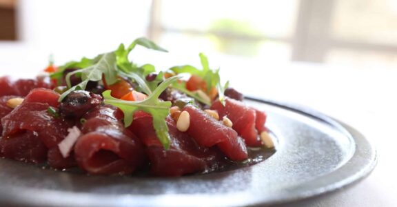 Carpaccio orné de roquette, légumes et pignons.